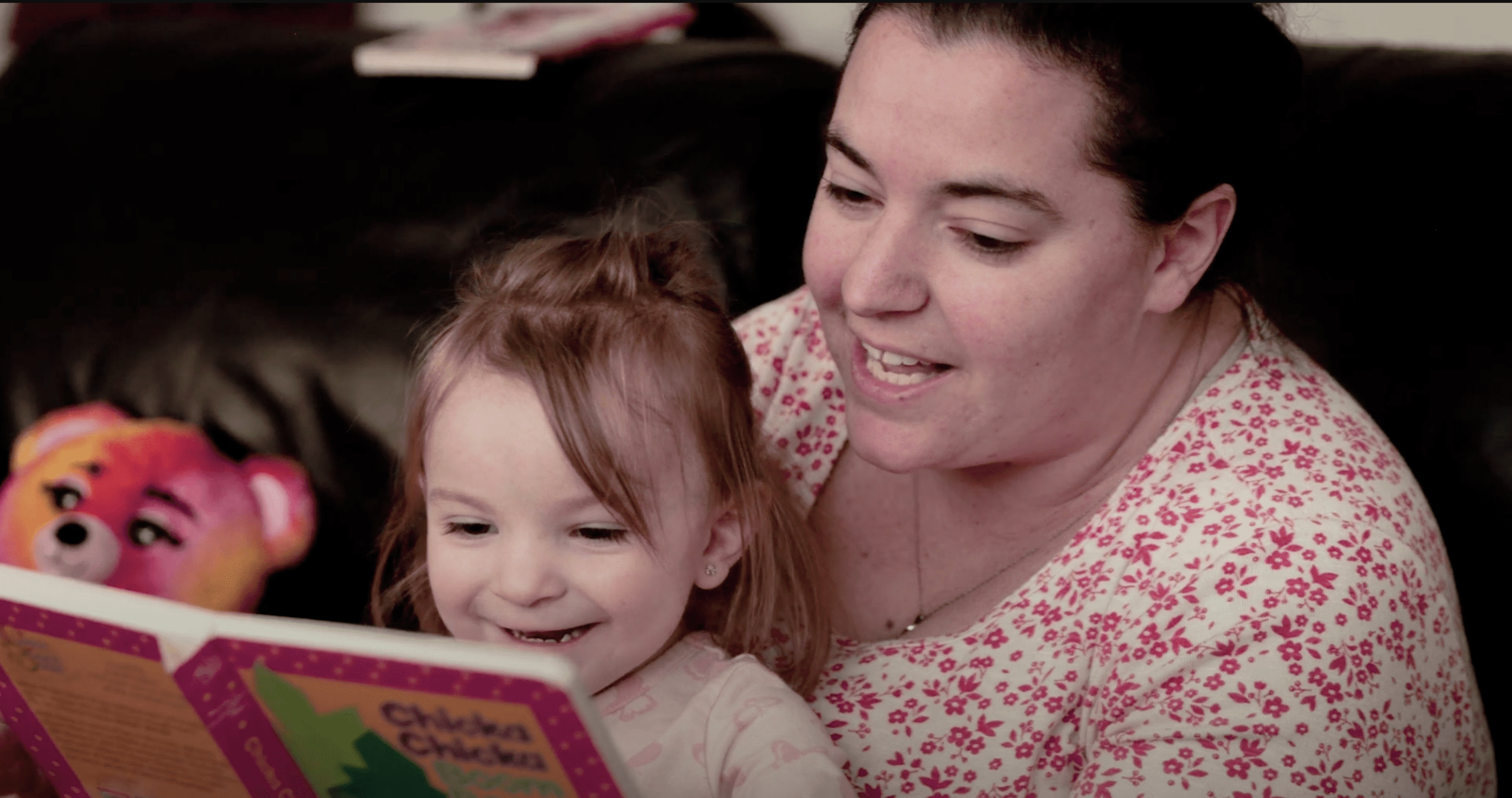 Winnie smiling while reading a book with her mom Tia on the couch